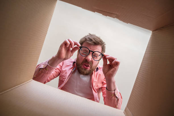 Strange man looks at the bottom of an unpacked delivered box with a parcel with a disappointed look. Unboxing inside view. stock photo