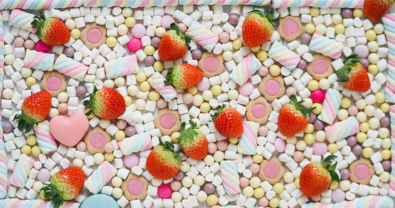 Strawberries and candies. Flatlay image of fresh strawberries and many pastel sweet including marshmallows, macarons, chocolate and candies. Food pattern background. focus on strawberries