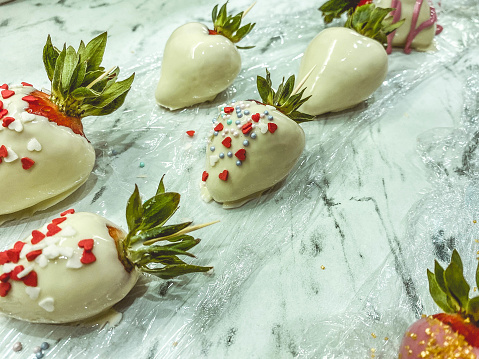 strawberries in chocolate on a marble background. sweet dessert, mouth-watering berries in milk white chocolate with sugar sprinkles in the form of hearts.