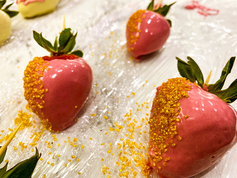 strawberries in chocolate on a marble background. sweet dessert, appetizing berries in milk pink chocolate with sugar sprinkles, caramel sweetness.