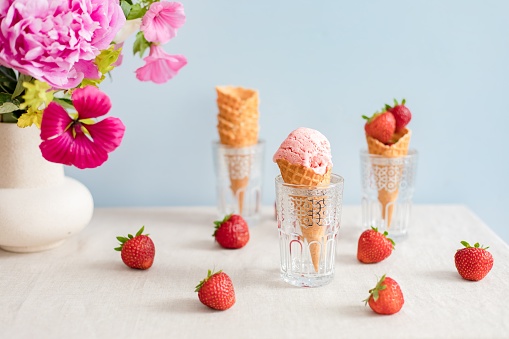 Strawberry icecream and fresh strawberries served in ice cream cones for a summer party with a beautiful pink floral arrangement.