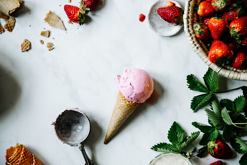 Top view of a strawberry ice cream in waffle cone on table. Strawberry ice-cream with strawberries in basket and ice cream scoop over a table.