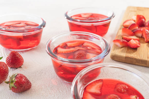 Strawberry Jelly in a Glass Bowls, Sliced Strawberries on a Chopping Board, Close Up, on White Background stock photo