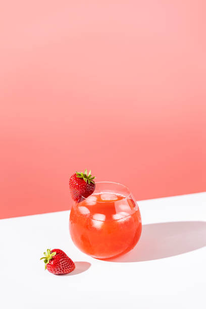 Strawberry mojito cocktail with ice in brandy glass with water drops  on pastel soft pink color background in bright sun light, white board. Copy space, summer vacation and party concept stock photo