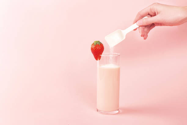 Strawberry smoothie and a spoon with collagen powder or protein. Woman pouring collagen powder or protein in strawberry smoothie or milk. Extra protein intake. Natural beauty and health supplement. Plant or fish based. Flatlay, top view. Copy space. collagen stock pictures, royalty-free photos & images