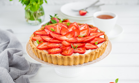 Strawberry tart with custard cream on a plate on a white wooden background. Copy space