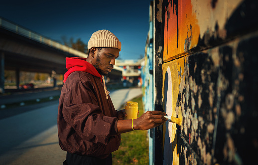 Closeup side view of a young African American man creating street art drawing on the wall.