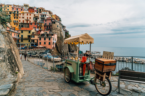 View of a street food stall on a bicycle in the street in the coastal old town of Manarola and houses on a hill in the background, Cinque Terre, Liguria, Italy