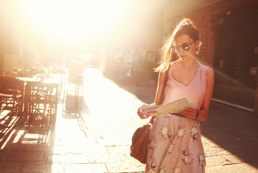 young brunette sightseeing on the street, looking at the map, lit by the magic hour sunlight.