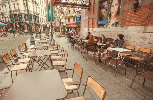 Brussels, Belgium - Apr 9, 2018: Street tables of outddor cafe with furniture, drinking people and old buildings with restaurants on April 9, 2018. More than 1,200,000 people lives in Brussels