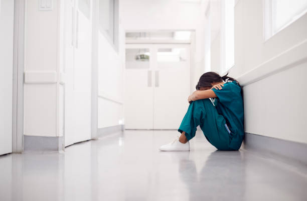 medico donna stressato e troppo lavoro che indossa scrub seduti sul pavimento nel corridoio dell'ospedale - stress foto e immagini stock