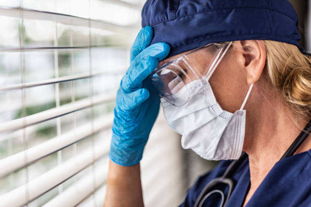 Stressed Female Doctor or Nurse On Break At Window Wearing Medical Face Mask and Goggles Stressed Female Doctor or Nurse On Break At Window Wearing Medical Face Mask and Goggles. frontline worker stock pictures, royalty-free photos & images