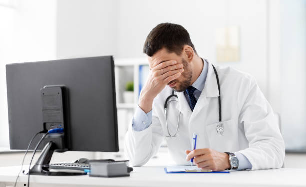stressed or tired male doctor with clipboard at hospital stock photo