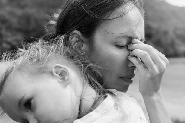 Stressed out sad mother holding her baby. Postpartum depression. A sad mother covering her face depressed and unhappy holding her child in black and white. struggle stock pictures, royalty-free photos & images