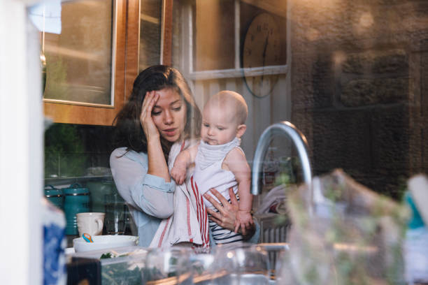 Stressed Single Mother Young mother is standing in her kitchen trying to make up baby food for her daughter, who she is carrying on her hip. struggle stock pictures, royalty-free photos & images