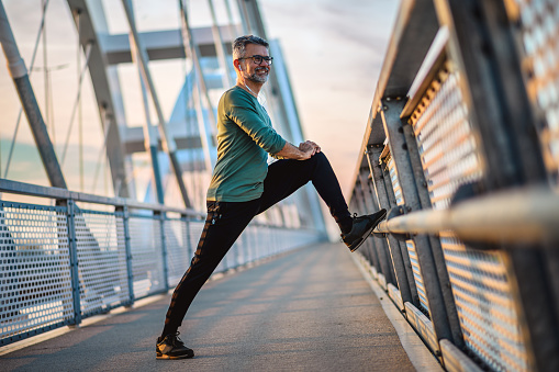 Mature sportsperson stretching his legs on a bridge walkway.