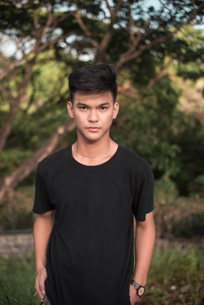 A strikingly handsome young Filipino man at the park. In a black t-shirt. At the park during late afternoon. stock photo