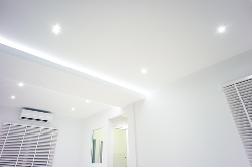 LED strip light and illumination. Also called ribbon light or LED tape. That suspended on ceiling and hide in plasterboard in empty living room include down light, white wall, window, air conditioner, adjusting vertical or venetian blinds. That is modern luxury interior home building design and technology.
