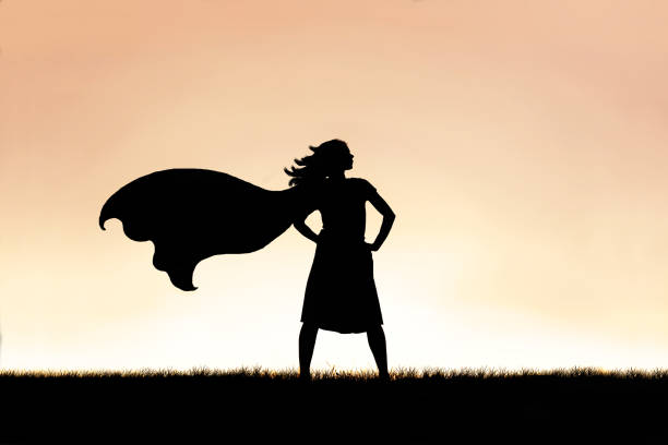 Strong Beautiful Caped Super Hero Woman Silhouette Isolated Against Sunset Sky Background The silhouette of a strong, beautiful caped super hero woman stands isolated against a sunset in the sky background. cape stock pictures, royalty-free photos & images
