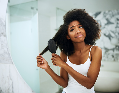 Shot of an attractive young woman struggling to comb her hair at home