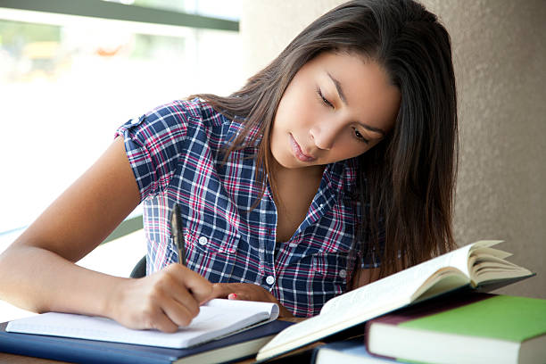 Student concentrating on writing in book with other books Pretty latin girl is doing her homework and wrting on a notebook. mexican teenage girls stock pictures, royalty-free photos & images
