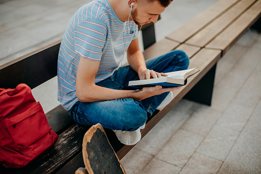 College student sitting outside on bench reading book