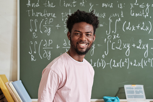 Portrait of African student smiling at camera standing against the blackboard with math formulas in the classroom