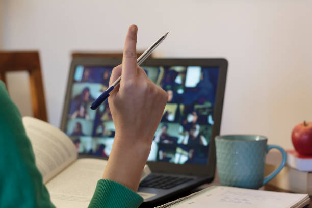 Student taking an online class with his arm raised to ask a question stock photo