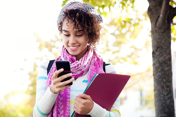 Student using a smart phone Ethnic woman with curly hair posing with a pink and fusia scarf and hat while using her cell phone and smiling. cute puerto rican girls stock pictures, royalty-free photos & images