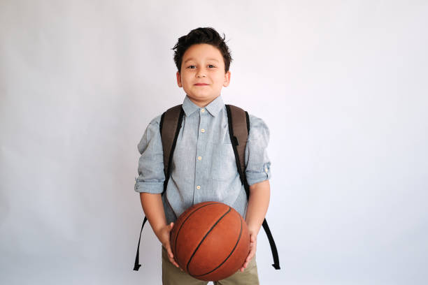 Student with fashionable clothing and school backpack on white background. Holding basketball ball stock photo
