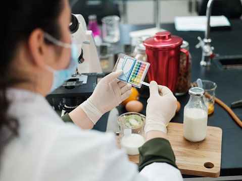 Female student wearing gloves and examining different foods in a laboratory.
