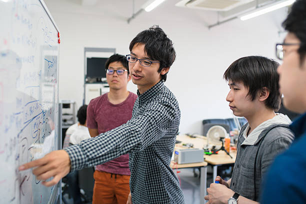 Students looking at scientific formula University students stood around a whiteboard looking at scientific formula and having a meeting. Kyoto, Japan. May 2016 game development stock pictures, royalty-free photos & images