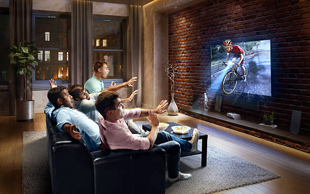 Students watching very realistic Cycle competition on TV :biggrin:A group of young male friends are shocked while watching very realistic Cycle competition game on TV. They are sitting on a sofa in the modern living room. The TV set is on the loft brick wall. It is evening outside the window. race sumilator stock pictures, royalty-free photos & images