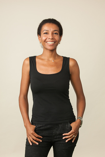 studio portrait of a 33 year old african american woman in black ttank top and black jeans on a beige background