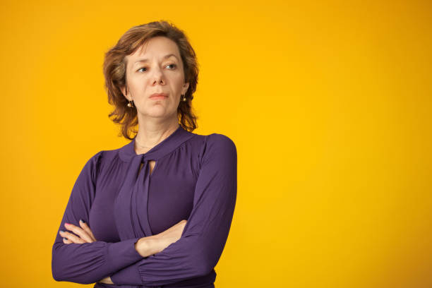 Studio portrait of a 40 year old woman in purple blouse on a yellow background Studio portrait of a 40 year old woman in purple blouse on a yellow background arrogance stock pictures, royalty-free photos & images