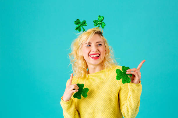 Studio portrait of a smiling woman holding shamrock  having fun and pointing up, with St. Patrick's Day head decoration stock photo