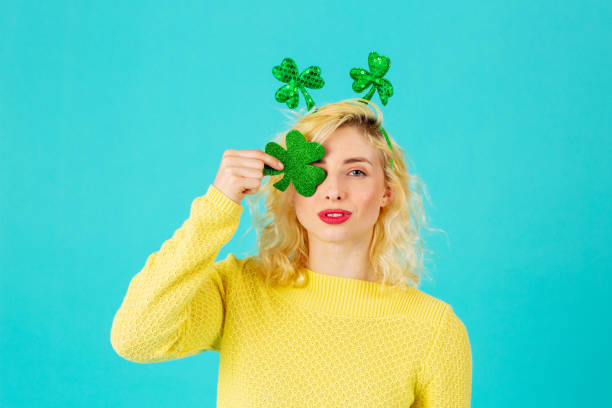 Studio portrait of a smiling young woman holding shamrock covering one eye, with St. Patrick's Day head decoration stock photo