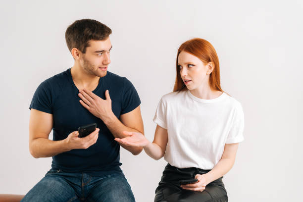 Studio portrait of frustrated woman angry to boyfriend using smartphone all the time without paying attention to her on white isolated background. stock photo