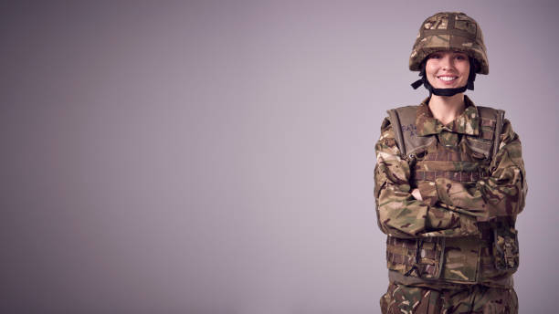 Studio Portrait Of Smiling Young Female Soldier In Military Uniform Against Plain Background stock photo