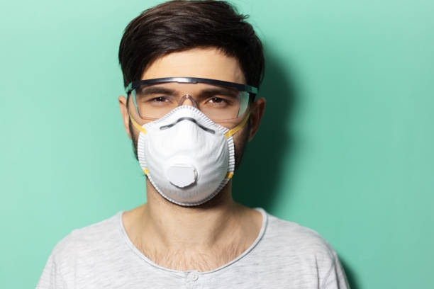 Studio portrait of young guy wearing medical face mask and protective goggles against coronavirus isolated on background of aqua menthe color. Studio portrait of young guy wearing medical face mask and protective goggles against coronavirus isolated on background of aqua menthe color. aqua menthe photos stock pictures, royalty-free photos & images