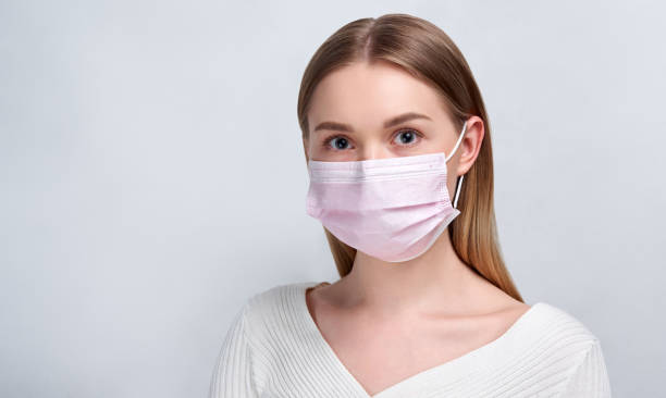 Studio portrait of young woman wearing a face mask, looking at camera, close up, isolated on gray background. Flu epidemic, dust allergy, protection against virus. City air pollution concept Studio portrait of young woman wearing a face mask, looking at camera, close up, isolated on gray background. Flu epidemic, dust allergy, protection against virus. Blonde woman costume stock pictures, royalty-free photos & images