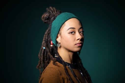 Close-up portrait of young african american woman with blank expression against green background. Real people staring with locs - hairstyle and headband.