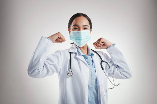 Studio shot of a female doctor wearing a mask and flexing while standing against a grey background stock photo