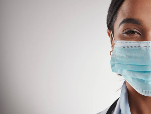 Studio shot of a female doctor wearing a surgical mask while standing against a grey background stock photo