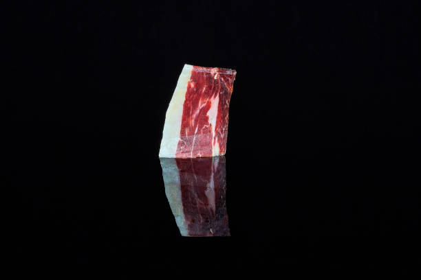 studio shot of a slice of 100% Iberian acorn-fed ham on a black background with the reflection. stock photo