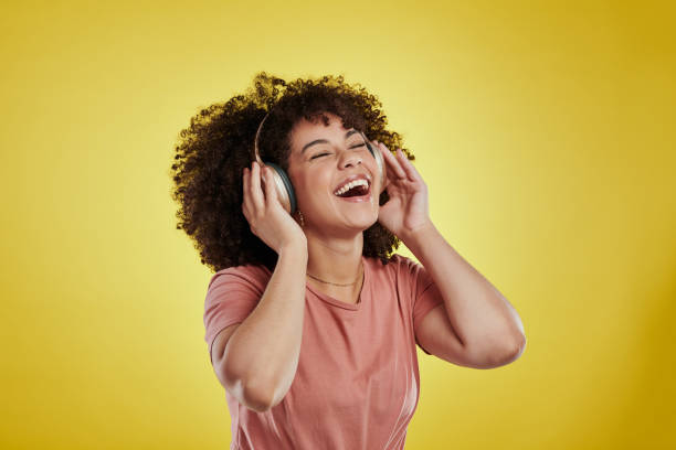 Studio shot of an attractive young woman using headphones against a yellow background stock photo