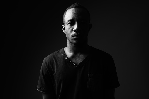 Studio shot of young African man wearing black shirt in black and white horizontal shot