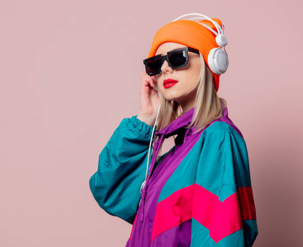 Style girl in 80s sportsuit and sunglasses with headphones on pink background stock photo