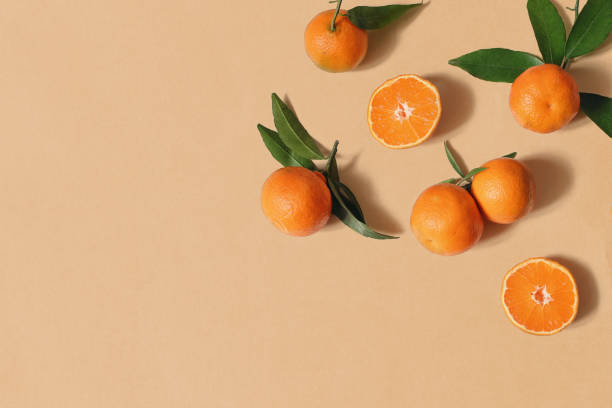 styled stock photo. decorative summer fruit composition. whole and sliced orange tangerines, citrus fruit and leaves isolated on orange table background. food pattern. empty space. flat lay, top view. - laranja imagens e fotografias de stock