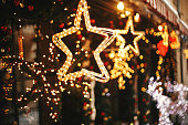 istock Stylish christmas golden star illumination and fir branches with red and gold baubles, golden lights bokeh on front of building at holiday market in city street. Christmas street decor 1175684792